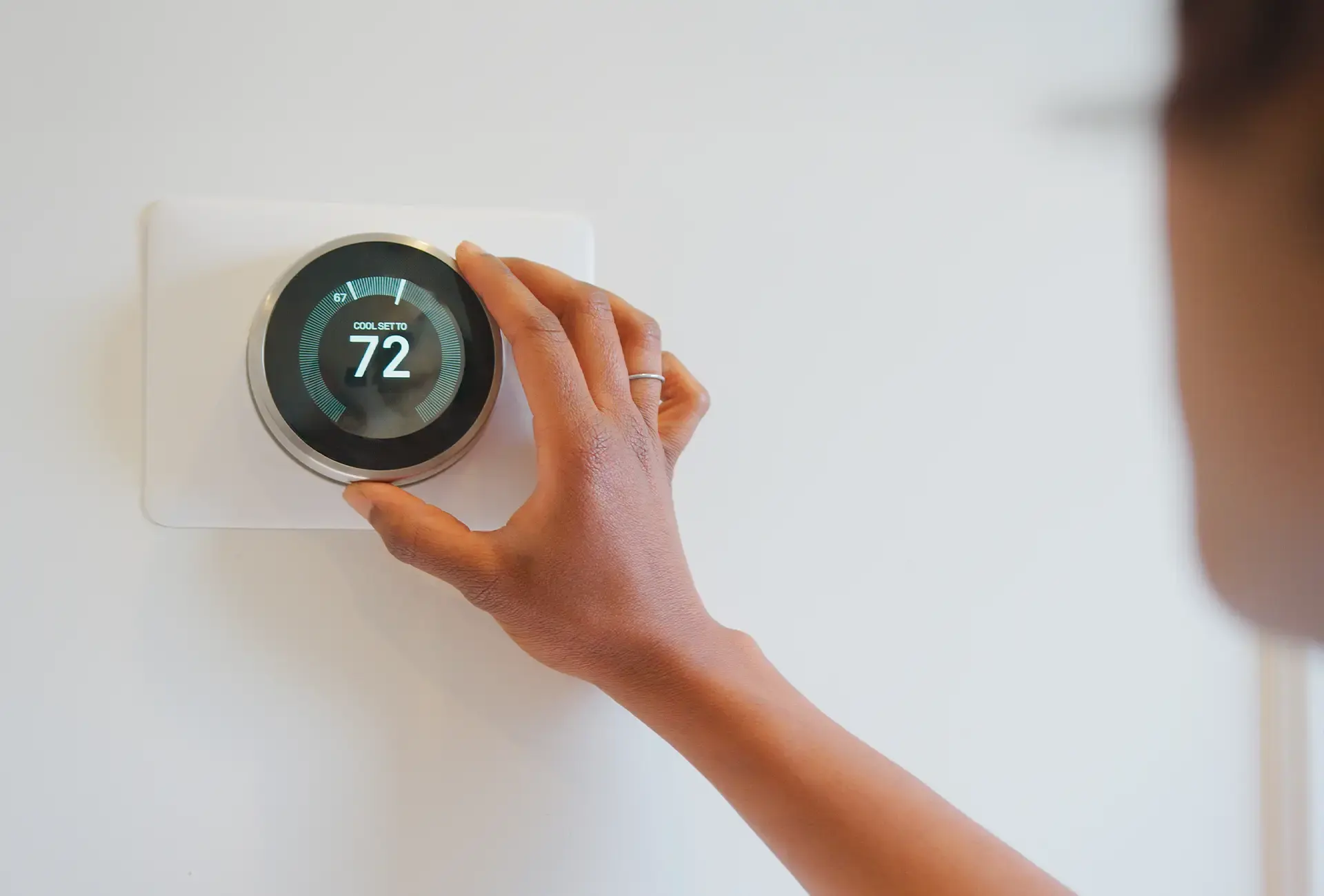 A person adjusting a domestic wall-mounted thermostat